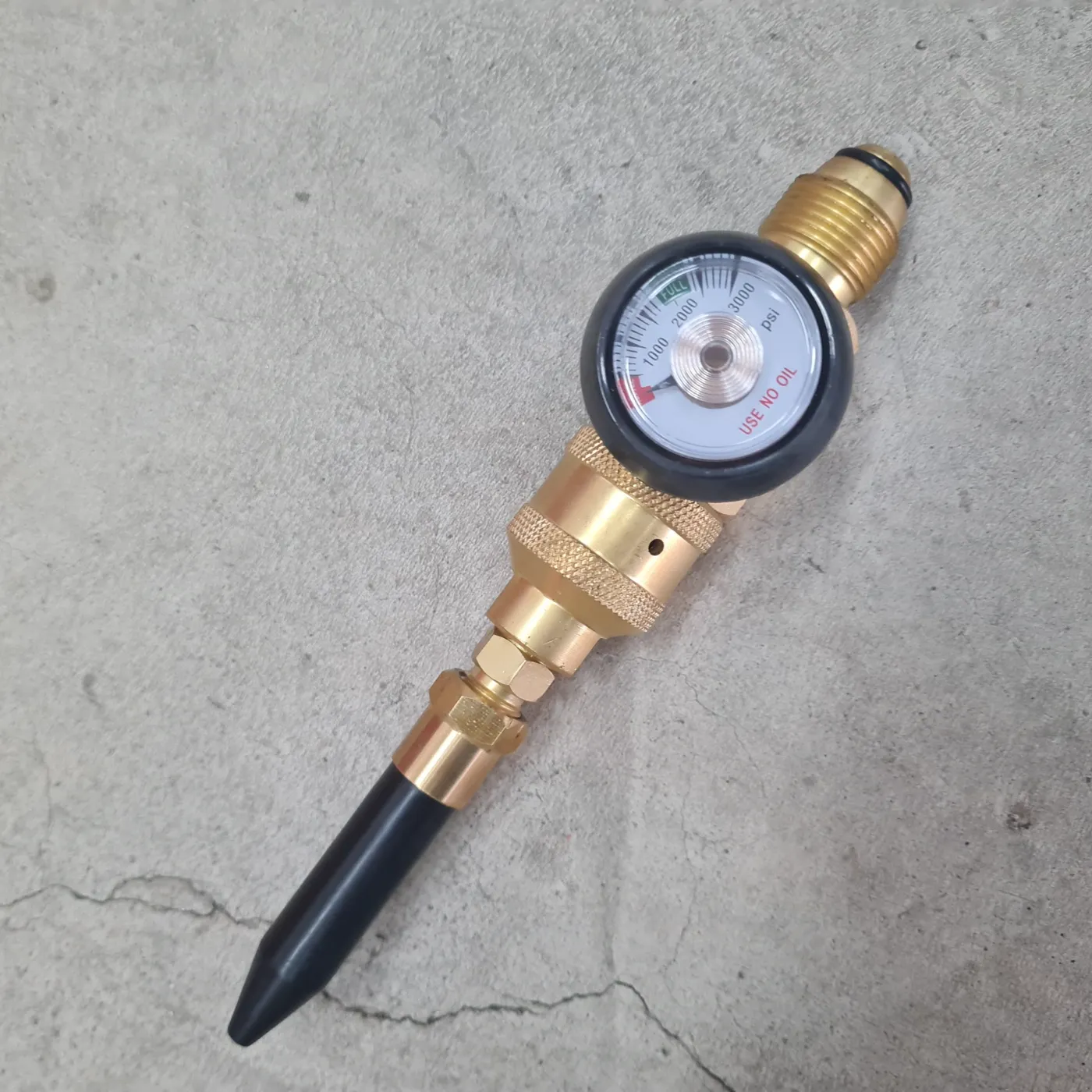 Brass cylinder pressure-testing gauge on the workshop floor at Airgas Nilai